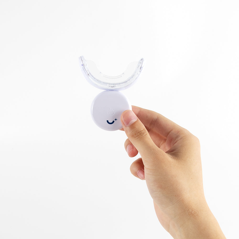 Close-up of a hand holding a Whitening Laboratory LED teeth whitening device, showcasing the modern design and ease of use for at-home dental care.